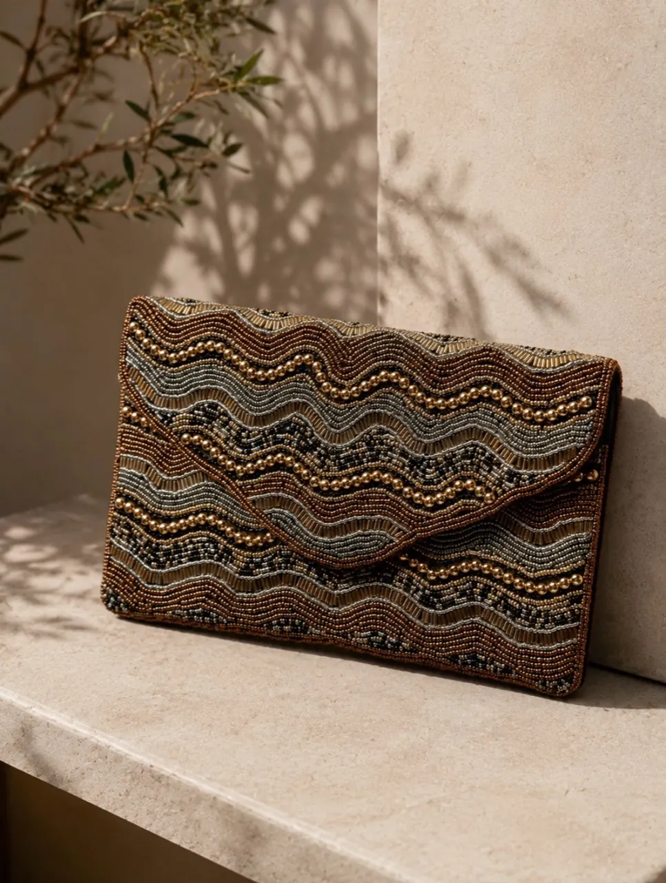 Clutch bordado en tonos chocolate y dorado sobre una superficie de piedra